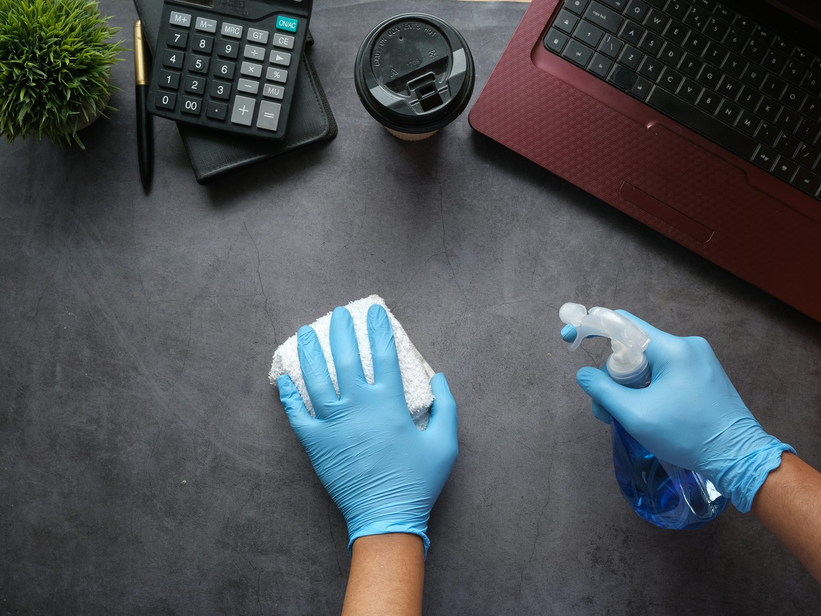 Agent en gants désinfectant un poste de travail au chiffon et au pulvérisateur